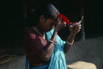 Young woman applying red sindoor paste to central parting of hair to signify that she is a married Hindu.Asia Asian Bharat Inde Indian Intiya Religion Religious Religion Religious Hinduism Hindus As...