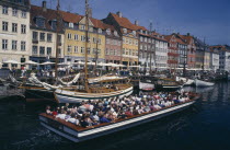 Nyhavn Canal. Cruise boat passing sailing boats moored on the quayside beside brightly painted traditional houses Danish Danmark Northern Europe Scandinavia
