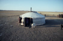 Ger or yurt in winter camp with dogs tied up outside and herdsman standing beside entrance.Asia Asian Mongol Uls Mongolian