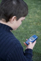 View over the shoulder of a boy holding a blue mobile phone with his thumb on the dialing pad.