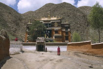 Labrang Monastery  elaborately designed building with a golden roof  partially obscured by a tree  and monks walking in the foreground.