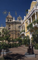 Plaza de San Pedro Claver.  Yellow and white colonial facade of building on right with part view of Church of San Pedro Claver beyond.  Sculpture and trees in foreground. Saint Peter Claver American...