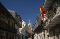 View along Calle San Pedro Claver towards cathedral bell tower and spire.  Narrow street lined with buildings with upper balconies  flags flying in foreground.Saint Peter Claver Colombian Columbia Hi...