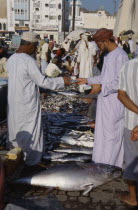Mutrah fish market.  Male vendor and customer making cash transaction over display of fish laid out on road.Middle East Omani United Arab Emirates Al-Imarat Al-Arabiyyah Al-Muttahidah Arabic Emiriti