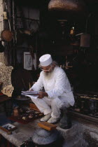 Elderly man wearing white sitting on step at entrance to antique shop to read papers.Bosnian European Male Men Guy Old Senior Aged Southern Europe Store Male Man Guy One individual Solo Lone Solitary