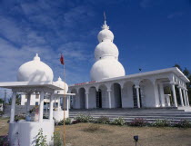 Hindu temple exterior with steps to colonnaded entrance and white  three dome spire above.  Small kiosks with statues in foreground.Indian Ocean African Eastern Africa Maurice Mauritian Religion Reli...