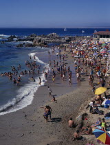 Crowded beach near Vina del Mar.  People sunbathing and playing in the surf.  Rocks and distant yacht beyond.American Beaches Chilean Hispanic Latin America Latino Resort Sand Sandy Seaside Shore South America Sunbather Tourism Tourists Travel Sunbathers