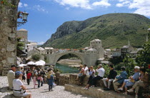 Stari Most  Old Bridge  following reconstruction  tourists  and Neretva River. Former YugoslaviaTravelTourismHolidayVacationAdventureExploreRecreationLeisureSightseeingTouristAttractionTourMostarBosniaHerzegovinaBalkanBalkansEuropeEuropeanTownCityHistoryHistoricHistoricalArchitectureArchitecturalSummerBrightSunnySunLandmarkYugoslaviaConstructConstructionStariMostOldBridgeNeretvaRiverHillHillsideSpanSpanningStructureConnectConnectionConnectingBridgingStoneArchWaterBridgedUNESCOWorldHeritageSiteRiversideReconstructionReconstructedRebuiltNewPeopleVisitorsTouristsSightseersMenWomenCobblesCobblestonesCobblestonedBusyStreetVacationBosnian Connexion Female Woman Girl Lady Male Man Guy Southern Europe Female Women Girl Lady Male Men Guy