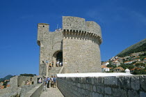 View along old city walls to Minceta Fort Tower and tourists. Former YugoslaviaTravelTourismHolidayVacationAdventureExploreRecreationLeisureSightseeingTouristAttractionTourMincetaDubrovn...