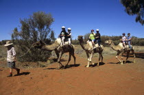 Kata Tjuta National Park  Camel train and riders  Mount Uluru  Ayers Rock.TravelTourismHolidayVacationAdventureExploreRecreationLeisureSightseeingTouristAttractionTourDestinationUluruKa...