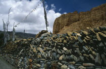 Prayer wall made from stacked stones engraved with prayers and with prayer flags flying above.Asia Asian Nepalese Religion Religious