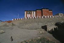 Red  grey and white exterior walls of Tsarang Monastery above flat roof adobe buildings with child on path in foreground.Asia Asian Gray Kids Nepalese Religion Religious gompa Children