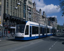 Damrak.  Blue and white tram on busy street partly obscuring shop  bar and hotel facades.  Pedestrians  marked cycle lane and modern street lights.North Benelux Dutch European Inn Netherlands Pub Sto...