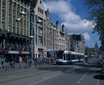 Damrak.  Busy street scene  lined with shop  bar and hotel facades.  Crowds of pedestrians  parked bicycles  marked cycle lane and blue and white tram.North Benelux Dutch European Inn Netherlands Pub...