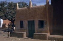 Traditional mud brick Hausa dwelling with men and boy beside exterior wall.African Kids Nigerian Western Africa Classic Classical Historical Male Man Guy Older History Male Men Guy