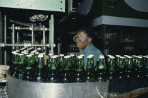 Brewery with man wearing safety goggles working  behind machinery and green glass bottles.African Male Men Guy Nigerian Western Africa Male Man Guy