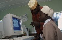 Teacher leaning over boy sitting at a computer in a classroomAfrican Kids Learning Lessons Nigerian Teaching Western Africa