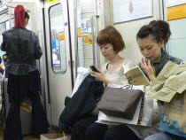 Ginza - three women on a subway train  right side young woman  shopping bags including Louis Vuitton  woman in the middle using cell phone text message  standing woman  left  with bright red pony tail...