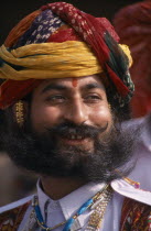 Head and shoulders portrait of a Rajput man smiling with a beard wearing ceremonial dress and a turban at the start of the Camel FestivalAsia Asian Nepalese Bharat Inde Indian Intiya Male Men Guy Mal...