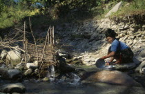 Woman washing pots beside a fish trap in a tributary river near Arughat VillageAsia Asian Nepalese Female Women Girl Lady Female Woman Girl Lady Clean Cleaning Laundry One individual Solo Lone Solita...