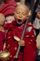 Young monk yawning during a ceremony and wearing red robes outside a small monastery in the back streetsAsia Asian Nepalese Bhadgaon Kids Religious Religion Immature One individual Solo Lone Solitary