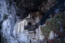 Holy Catholic cave shrine in rock face above waterfall and pool.  Contains sarcophagus of the Pelayo who defeated the moors in 718 AD.  People partly seen sitting outside.edge of Picos de Europa Nati...