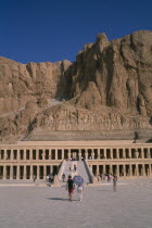 Deir el-Bahri. Hatshepsut Mortuary Temple. Visitors walking towards ramped entrance with limestone cliffs behindAfrican Middle East North Africa History Religion Religious