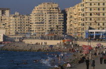 Corniche Waterfront seen in golden light. Busy beach with people swimming in the sea  fishing from the waters edge and walking on the promenade. Overlooked by tall buildings.El CornicheAfrican Middl...