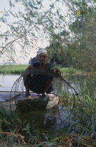 Nile Fisherman crouching down next to river bank on the West Bank under tree branches displaying his catch of fishAfrican Middle East North Africa One individual Solo Lone Solitary