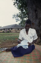 Young female teacher marking exam papers outside.African Eastern Africa Learning Lessons Teaching Ugandan Immature One individual Solo Lone Solitary