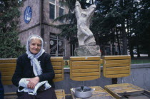 Elderly woman selling sunflower seeds from wooden seating infront of carved stone statue.Armenian Asia European Asian Middle East Female Women Girl Lady Old Senior Aged Female Woman Girl Lady One ind...