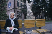 Elderly woman selling sunflower seeds from wooden seating infront of carved stone statue.Armenian Asia European Asian Middle East Female Women Girl Lady Old Senior Aged Female Woman Girl Lady One ind...