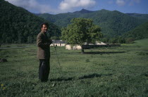 Man standing in rural landsape with low  stone building behind.Armenian Asia European Asian Middle East Male Men Guy Scenic Male Man Guy One individual Solo Lone Solitary