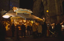 Breitscheidplatz. Christmas Market. People gathered around an Illuminated stall selling Feuerzangenbowle a German alcoholic drink made with wine  rum and sugar loaf.  A Christmas tree with a star near...