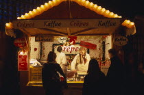 Breitscheidplatz. Christmas Market. Customers waiting at food stall illuminated at night cooking and selling Crepes  Coffee and Gluhwein which is similar to mulled wine.Pancakes Deutschland European...