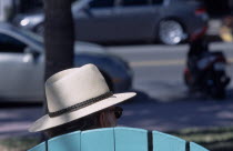 South Beach. Ocean Drive. The head of a man wearing a Panama hat seen above the top of a seat watching people and traffic go byAmerican North America United States of America Beaches Central America...
