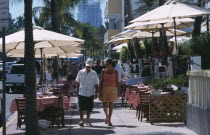 South Beach. Ocean Drive. A man and woman walking past a sidewalk cafe restaurant with table and chairs under sun umbrellasAmerican North America United States of America Bar Beaches Bistro Resort Sa...