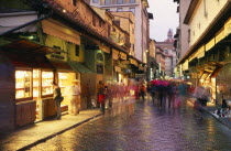 Street scene at dusk with shop fronts lining Ponte Vecchio  crowds in blurred movement and lights reflected on wet paving.European Firenze Italia Italian Southern Europe Store Toscana Tuscan