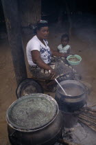 Woman cooking over wood burning open topped stove and passing helping of food to small girl sitting beside her.African Female Women Girl Lady Ghanaian Kids Western Africa Female Woman Girl Lady