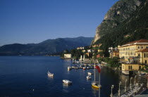 Waterfront buildings overlooking moored boats with mountain landscape behind.European Italia Italian Scenic Southern Europe