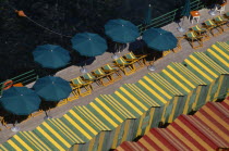 View over green and yellow and red and yellow striped beach huts  green and yellow striped deck chairs and green sun umbrellas on wooden decking.Beaches European Italia Italian Resort Sand Sandy Seas...