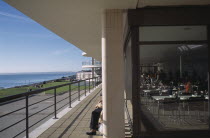 De La Warr Pavilion. View along the sun terrace next to the restaurant with people sitting on benches behind a pillar looking out to the sea.Commissioned by the 9th Earl De La Warr in 1935 and design...