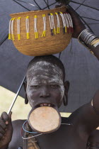 Woman with lip plate holding umbrella to shelter from sun with basket on head