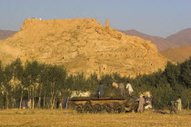 Children playing on abandoned tanks in fied in front of Ruined citadel of Shahr-e-Gholgola known as City of the Screaming   Destroyed by Genghis Khan in 1221 A.D. - the screams of its people as they were slaughted gave it its name but it is also know as the City of noise