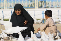 Lady wearing burqa and son feeding famous white pigeons at Shrine of Hazrat Ali  who was assissinated in 661 This shrine was built here in 1136 on the orders of Seljuk Sultan Sanjar  destroyed by Gen...