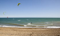 Kite Surfers on sea next to shingle beach in the summer with blue sky
