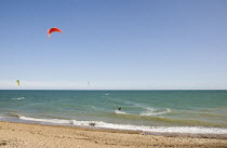 Kite Surfers on sea next to shingle beach in the summer with blue sky