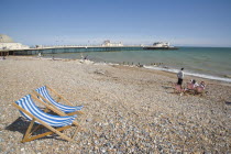 View across beach towards the pier with blue and white deckchairs in the foreground and sunbathers enjoying the sunshine nearby