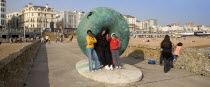 Tourists posing for photographs next to sculture on the seafront.