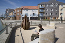 Ropetackle housing development on the banks of the river Adur. Young woman reading a book on the riverbank promenade. A regenerated brownfield former industrial area.